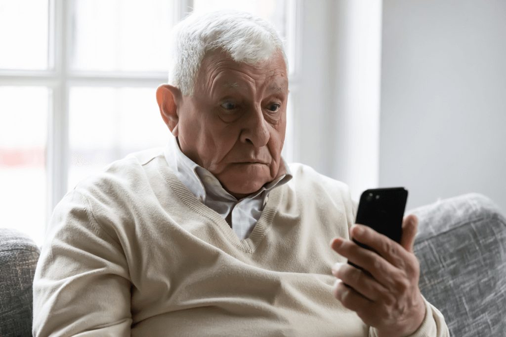 The older man sitting on couch and looking mobile