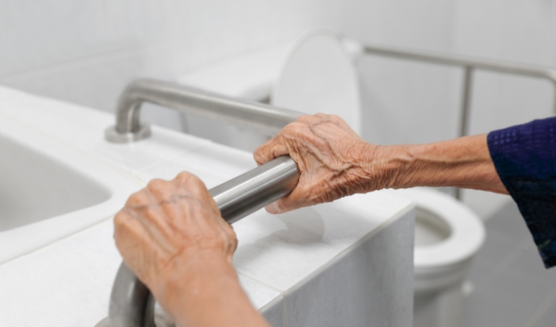 Older person holding grab rail in bathroom