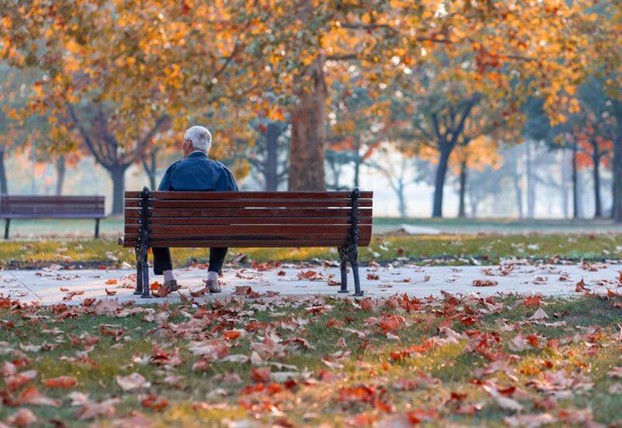 An elderly man sits alone in a park