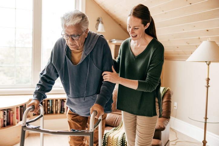 A woman assisting an elderly man using a walker indoors in Maryland & Washington, DC